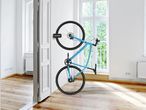 A blue bicycle mounted vertically on a white wall with an EASYmaxx Universal Bicycle Mounting Bracket.