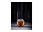 Steaming glass teapot filled with amber tea, set against a dark, reflective background.