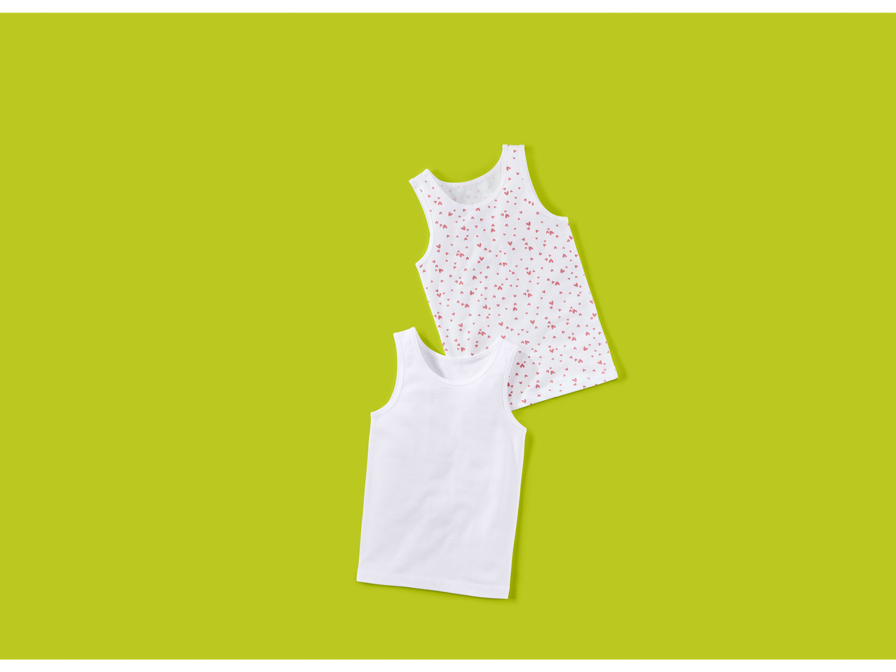 Dve dečije majice bez rukava, jedna bela i jedna bela sa roze srcima, na zelenoj pozadini.