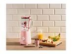 Pink blender with berries and yogurt, fresh fruit, and juice on a wooden counter.
