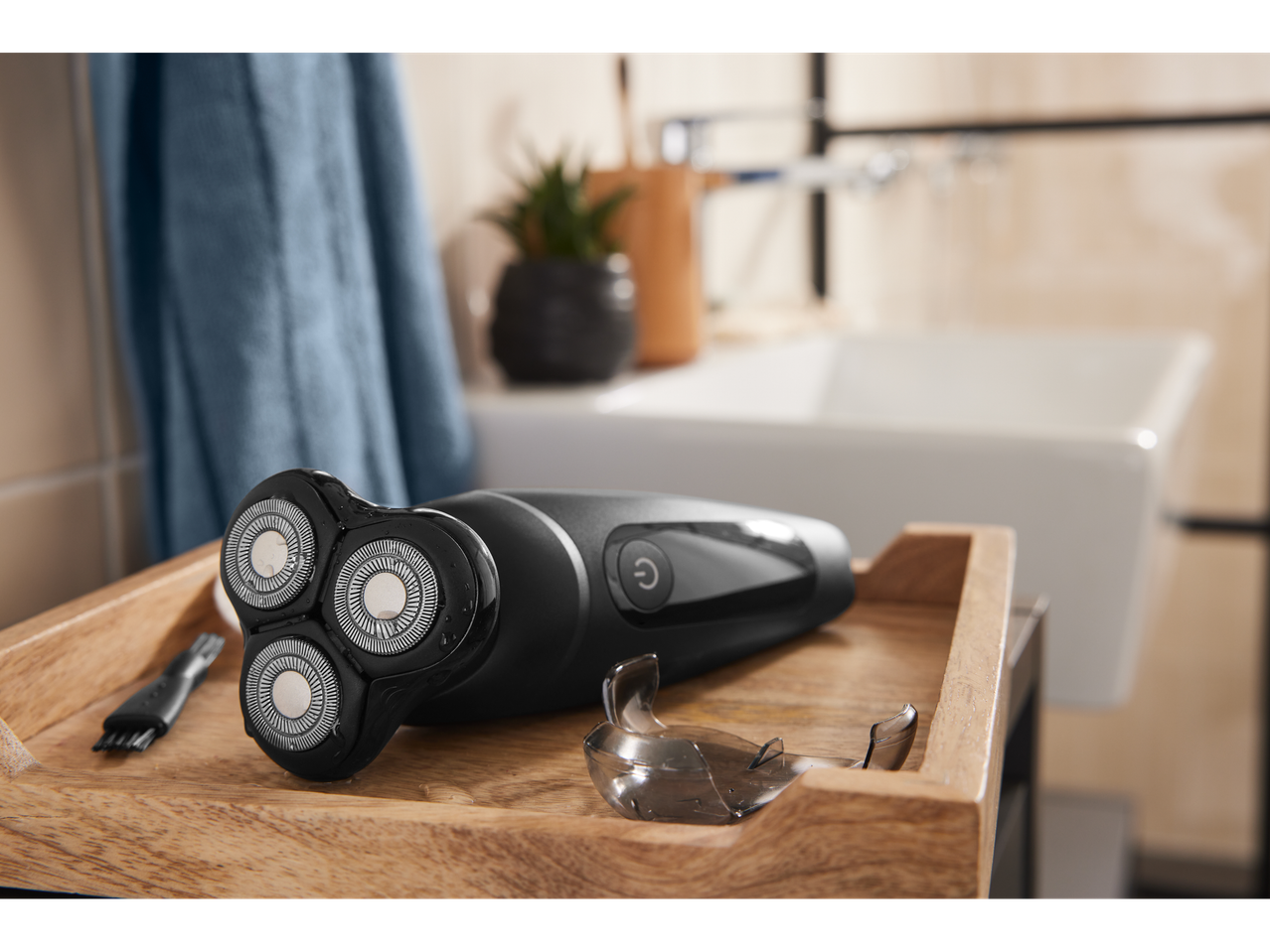 Um barbeador elétrico preto de três cabeças em uma bandeja de madeira em um banheiro.