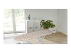 Ironing board with a beige leaf pattern cover in a bright room with a large window.