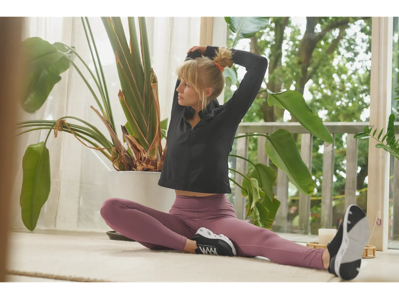 Moteris su juodu Crivit džemperiu ir violetinėmis tamprėmis mankštinasi ant grindų.