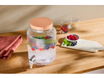 Dozator de băuturi din sticlă cu apă infuzată cu fructe, fructe de pădure și mentă pe un blat de lemn.