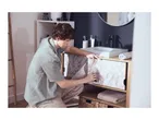 Man applying marble-effect adhesive film to bathroom cabinet doors, with a sink and mirror in the background.