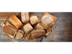 Assortiment de pains : pain blanc, pain complet et pain aux céréales sur une table en bois.