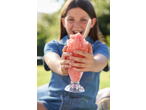 Fată zâmbitoare ținând un granita roz într-un pahar, în aer liber.