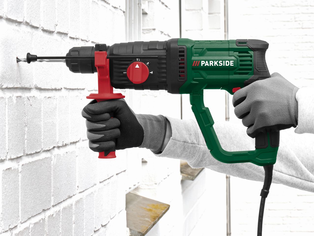 Person drilling into a white brick wall with a green and black rotary hammer drill.