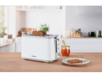 White toaster with two slices of seeded bread, a jar of jam, and a jam-covered slice on a plate.