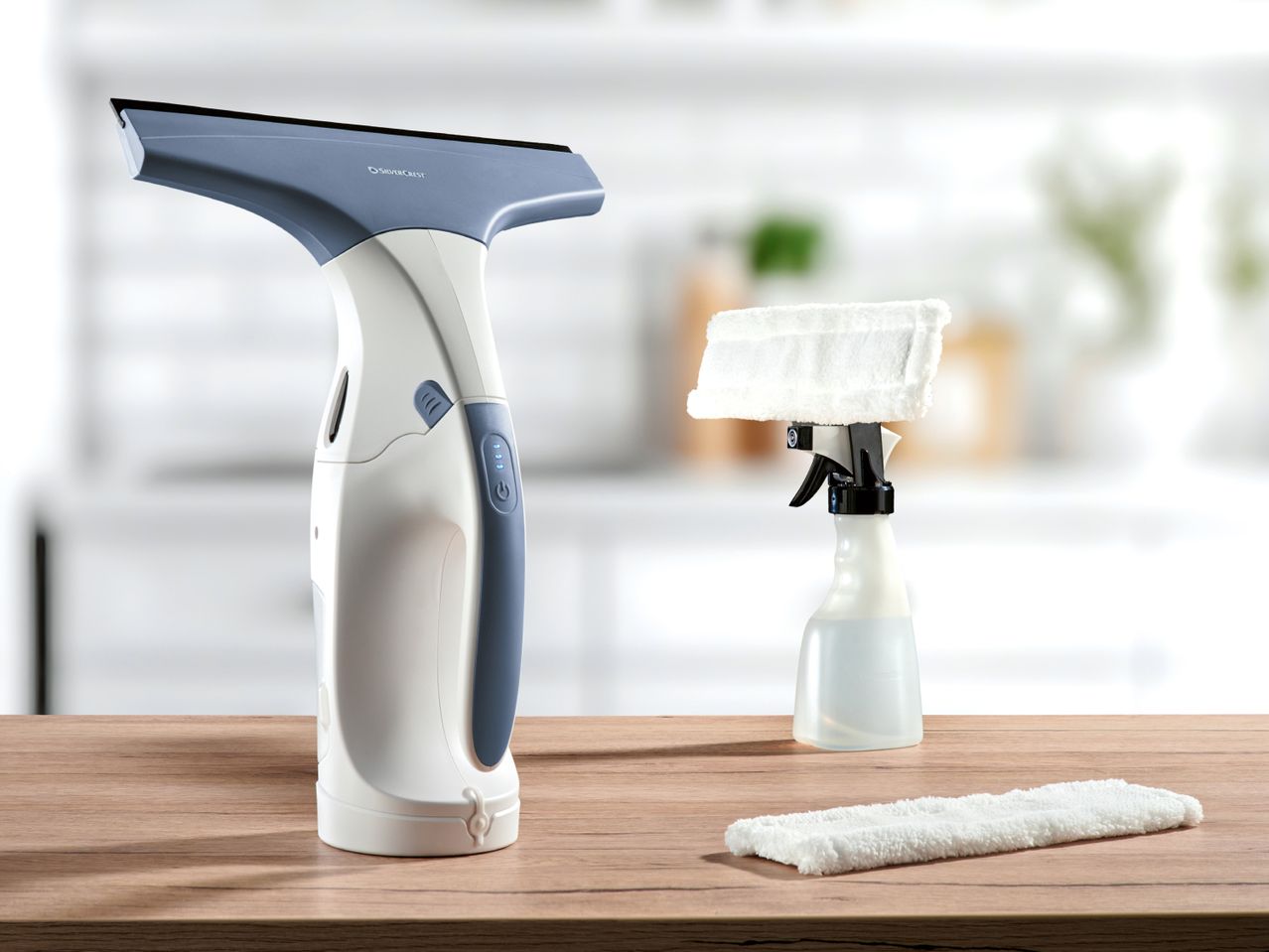 Window vacuum cleaner, spray bottle with microfiber pad, and an extra microfiber pad on a wooden table.