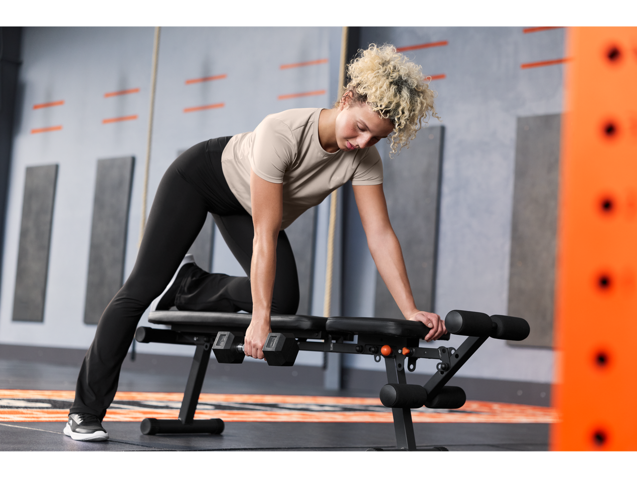 Woman in Crivit® sports shirt and leggings doing a dumbbell row on a bench.