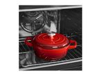 Red cast iron pot with lid inside an oven on a metal rack.