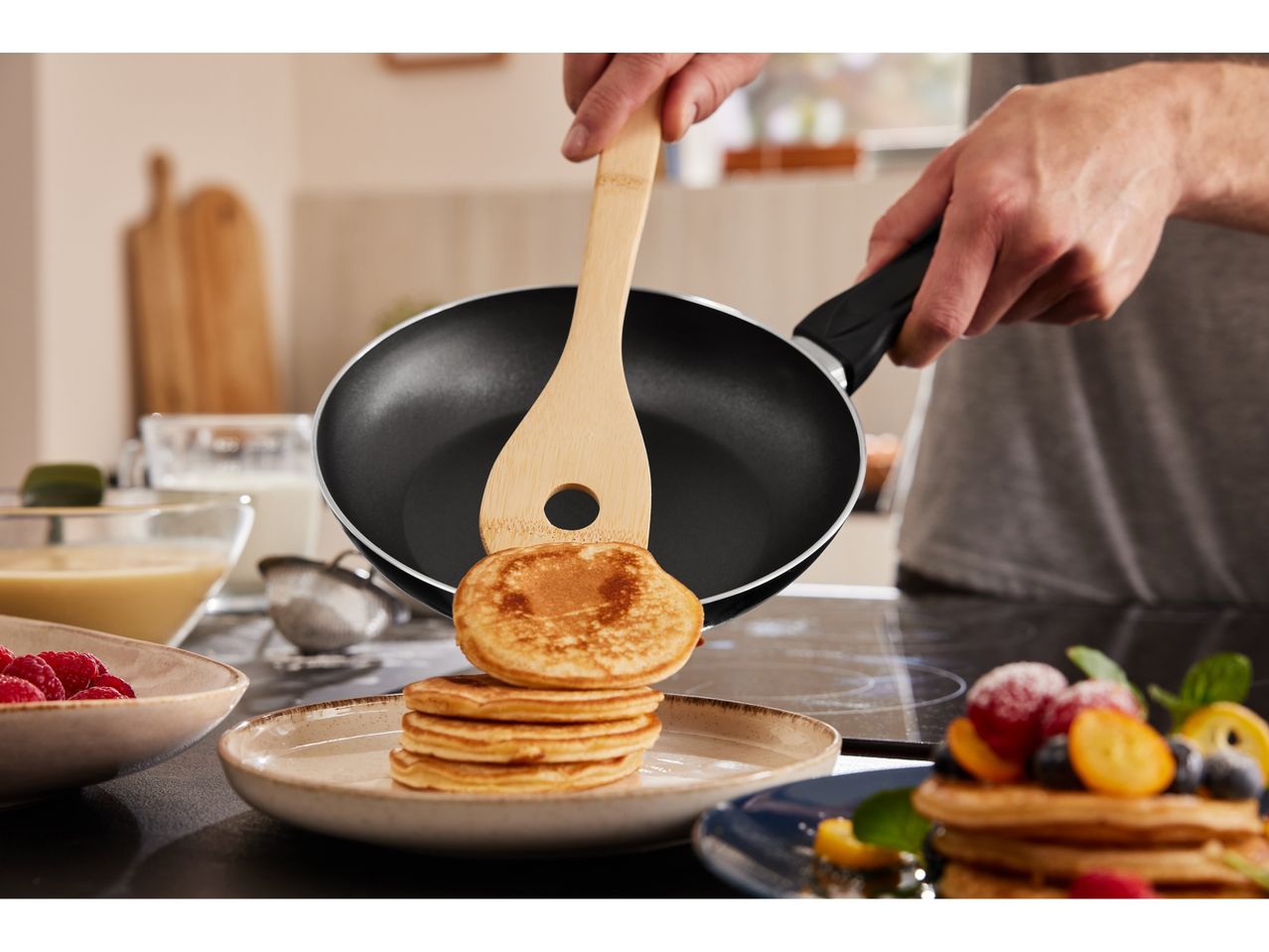 Wooden spatula flipping pancakes in a non-stick frying pan.