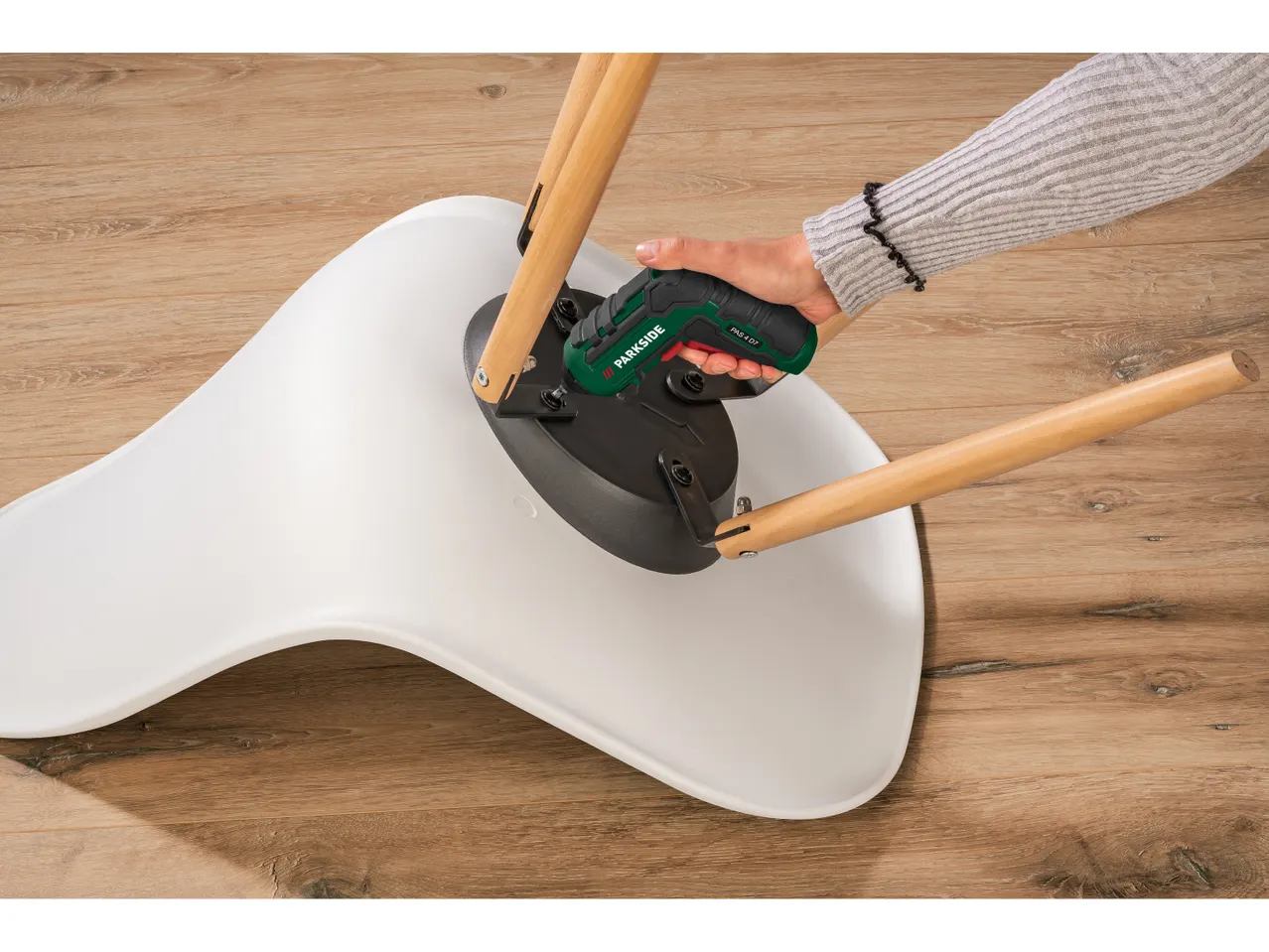 Una persona utilizza un avvitatore elettrico Parkside per assemblare una sedia moderna.