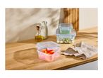 Food storage containers with chopped peppers, peas, and salad on a wooden counter.