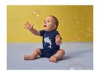 Baby in a blue shark-themed romper reaching for a bubble on a yellow and blue background.