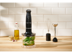 Crni štapni mikser s prozirnom posudom sastojaka za pesto na drvenoj radnoj ploči.