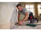 Um homem usa uma chave de fendas de catraca PARKSIDE para fixar um rodapé, com um conjunto de bits ao lado.