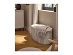 A light gray storage ottoman with a blanket on top, next to a window and a white cabinet.