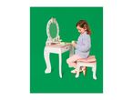A young girl playing with a white and pink wooden toy dressing table and stool.
