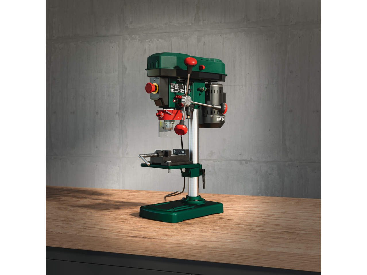 A Scheppach bench drill press sits on a wooden workbench against a concrete wall.