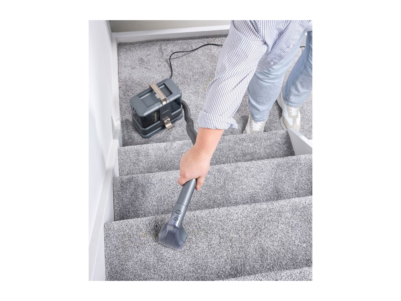Person cleaning light grey carpeted stairs with a portable spot cleaner.