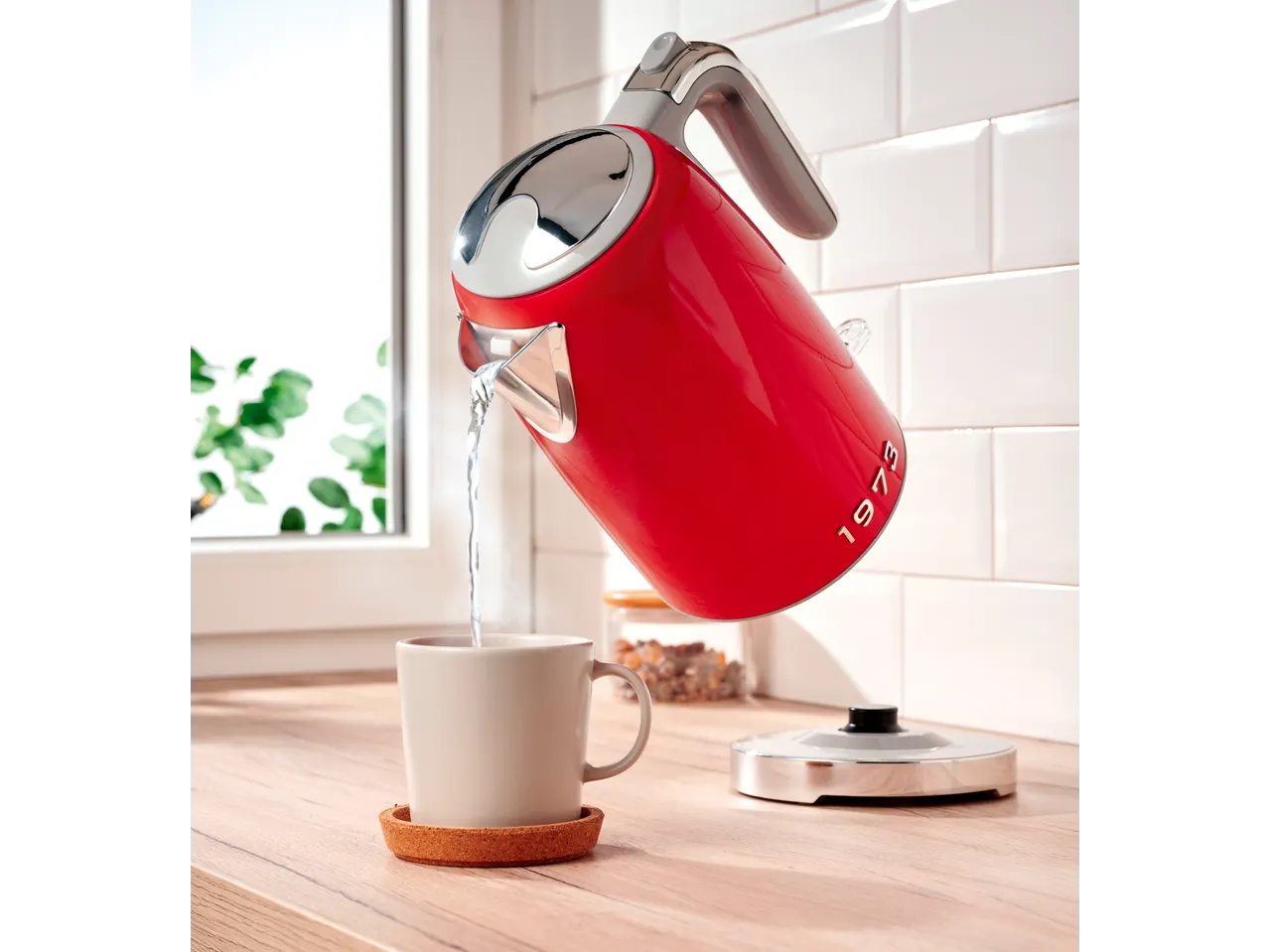 Red SILVERCREST® kettle pouring water into a mug on a wooden counter.
