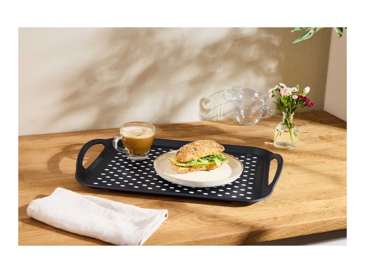 Breakfast tray with coffee, sandwich, and flowers on a wooden table.