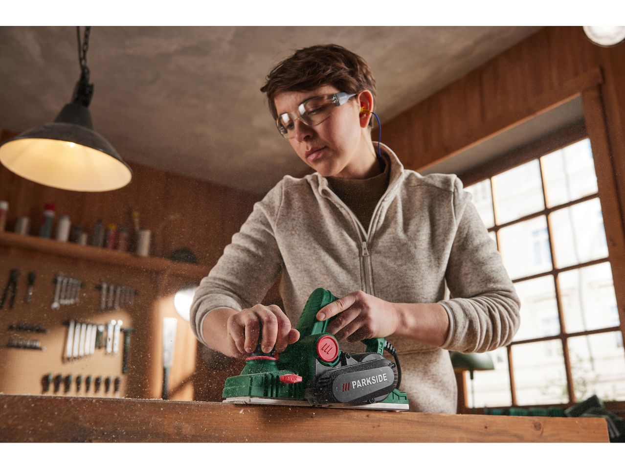 Una persona usa una pialla elettrica Parkside per lavorare il legno in un laboratorio.