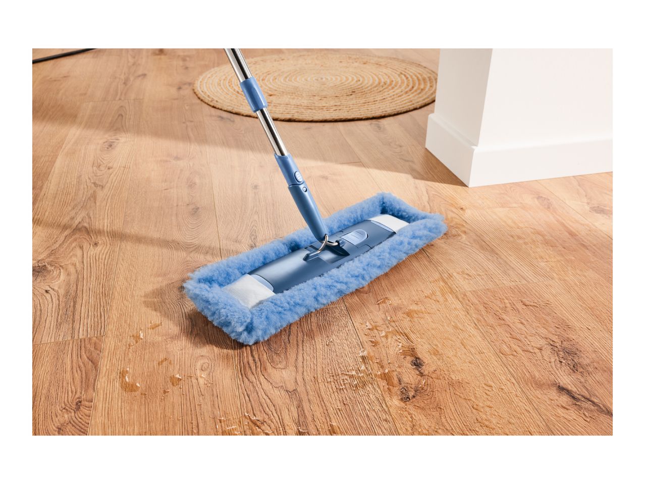 Blue mop cleaning a wooden floor with water spills