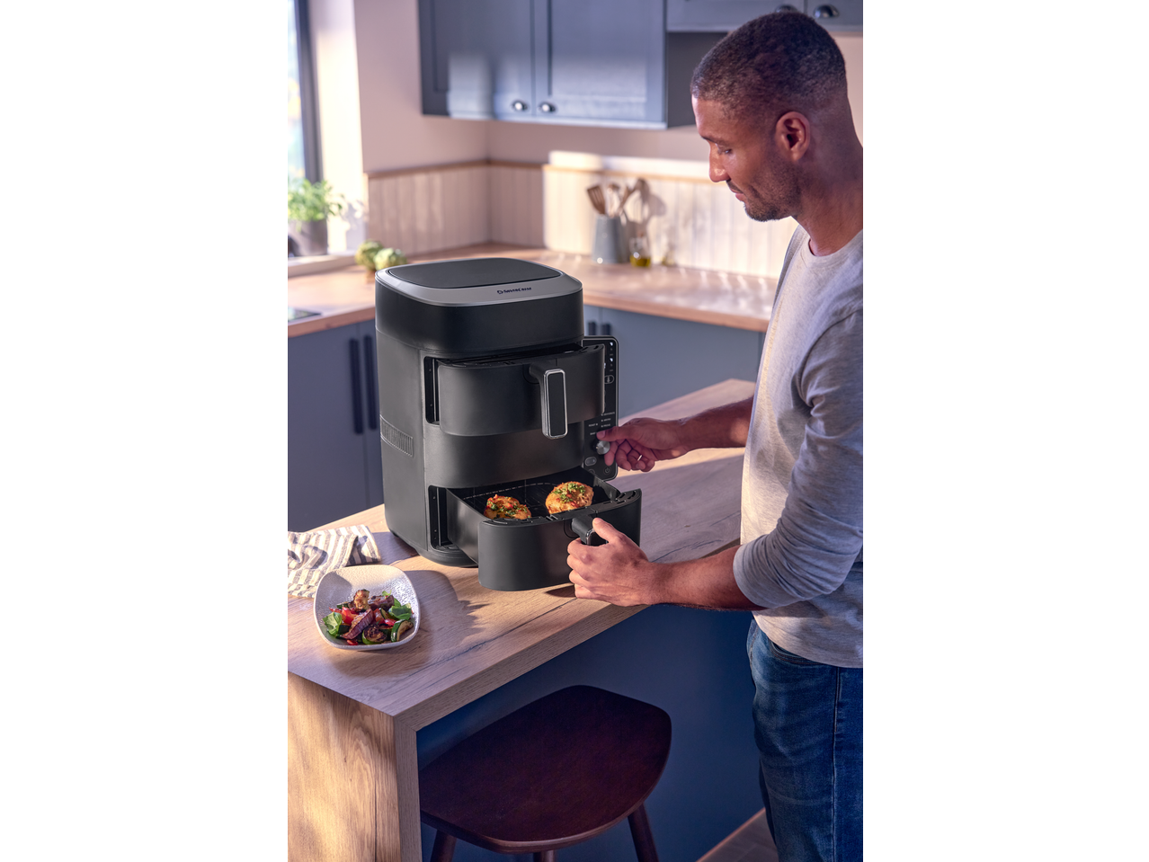 Man using a black air fryer with two baskets, cooking chicken and vegetables.