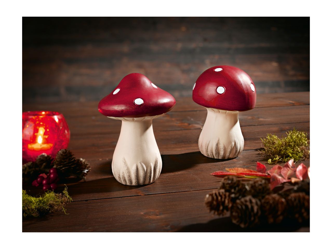 Two decorative red and white mushrooms on a wooden surface with autumn decor.