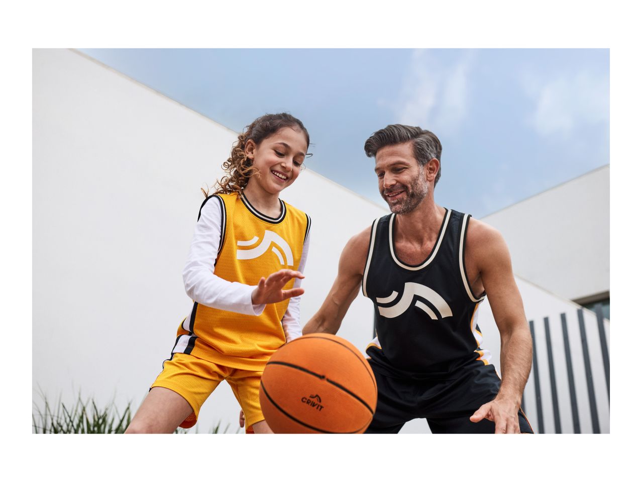 Father and daughter playing basketball in matching sports jerseys and shorts.