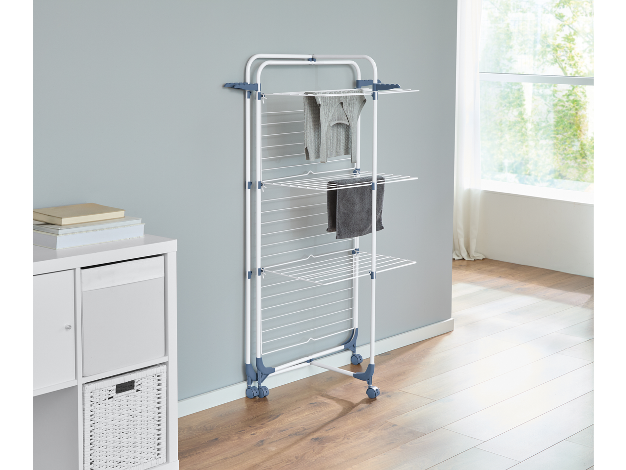 White and blue clothes drying rack with clothes on it, next to a white storage unit.