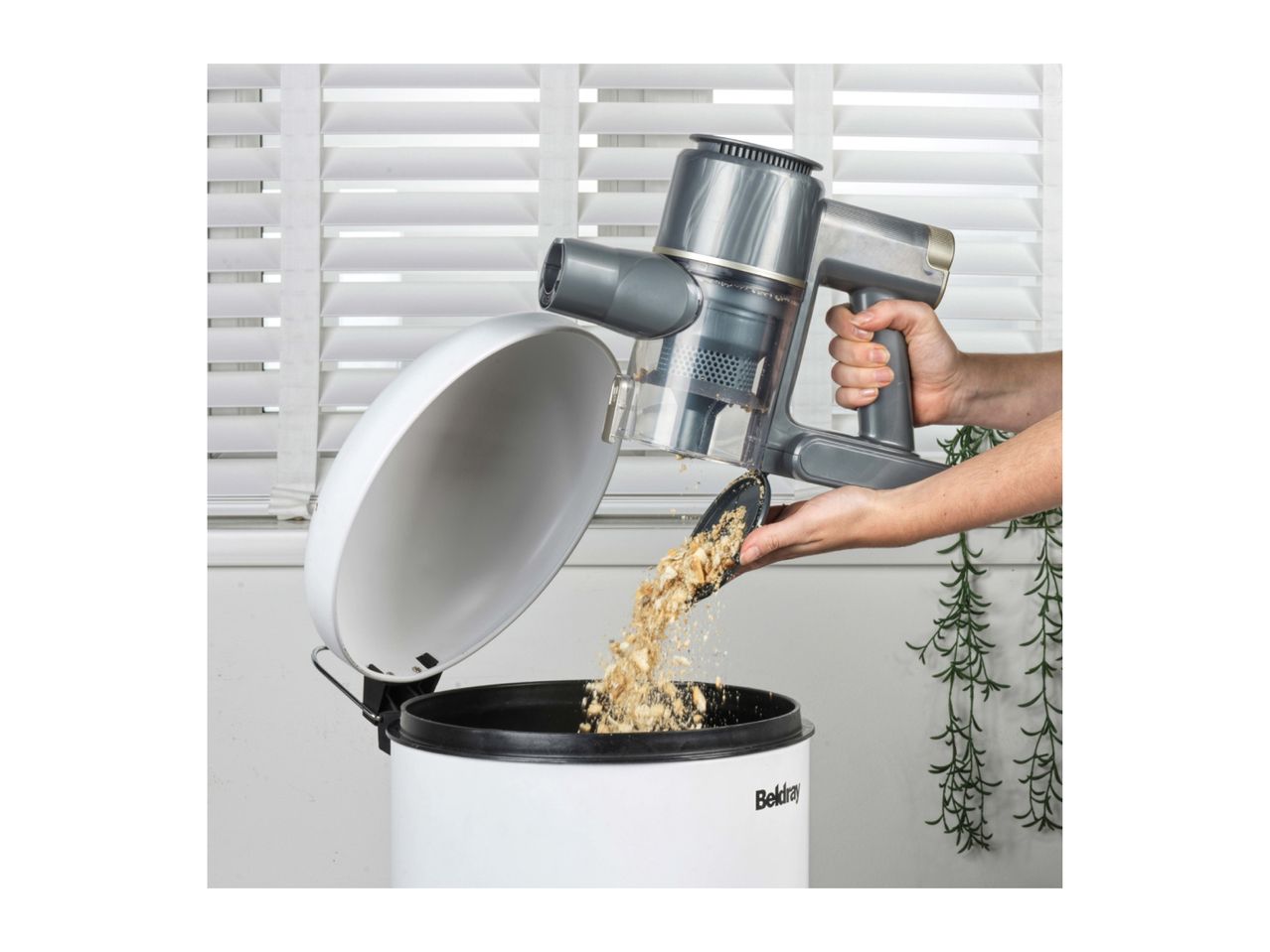 Handheld vacuum cleaner emptying crumbs into a white bin with a lid.