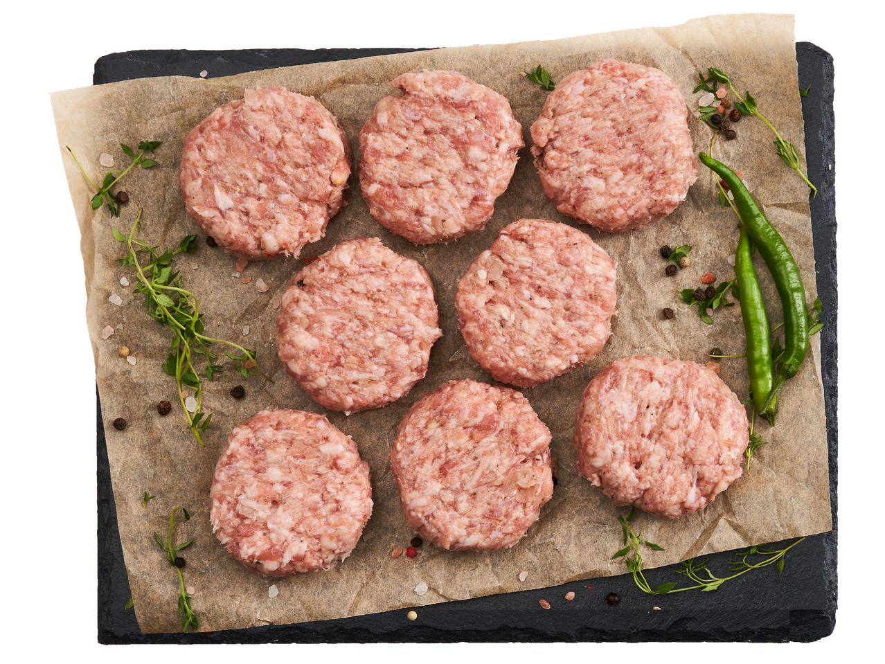 Сурови пилешки бургери с подправки и зелени люти чушки върху хартия за печене.