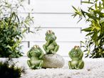 Three frog  for Garden Ornament with crowns on white gravel, surrounded by green plants.