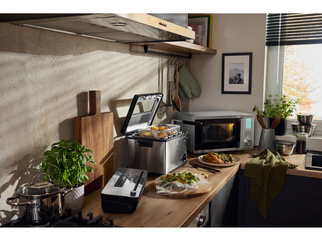 Cozinha com fritadeira, micro-ondas e seladora a vácuo em bancada de madeira.