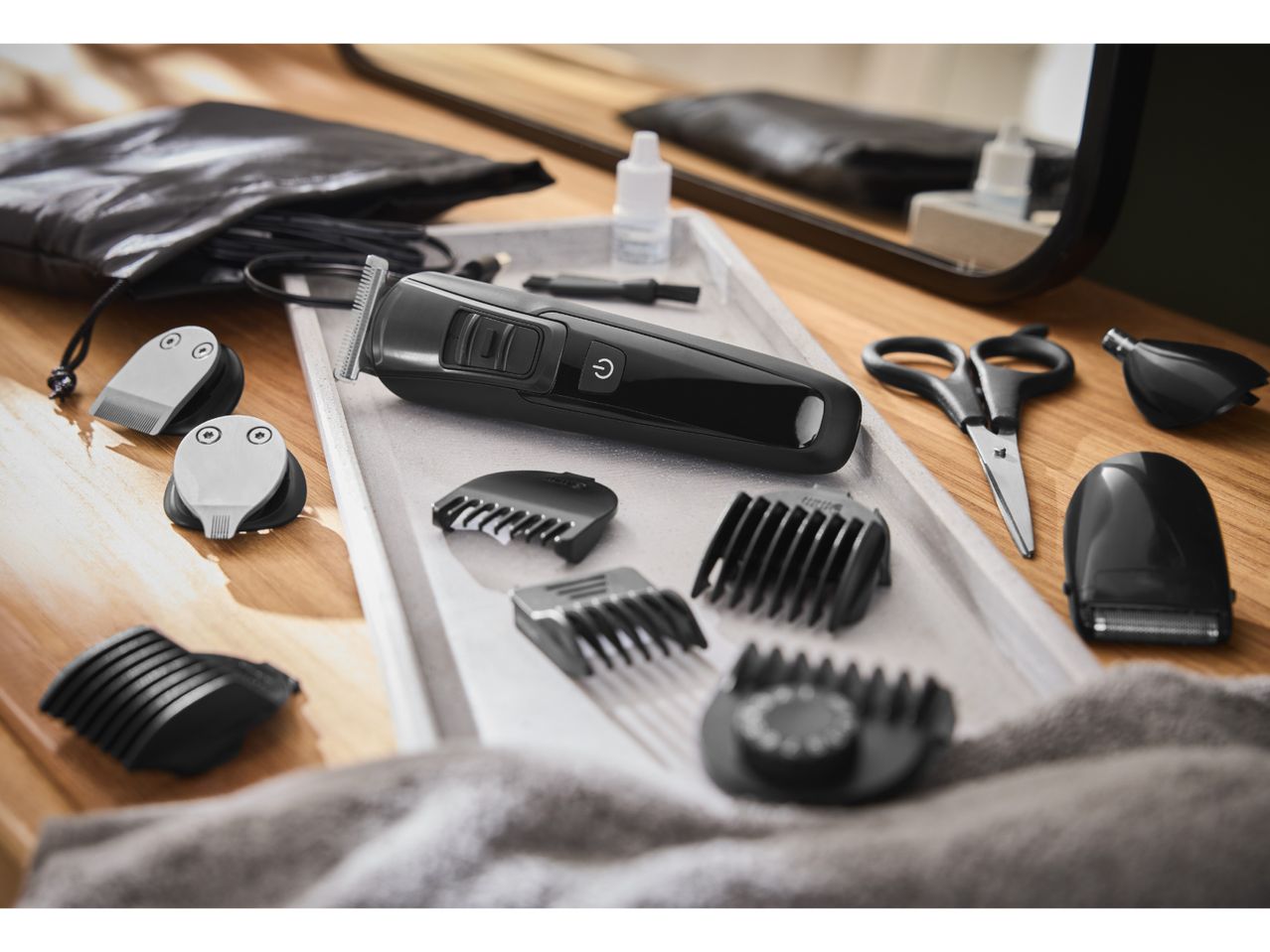 Hair trimmer set with various attachments, scissors, and oil on a wooden surface.