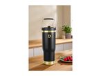 Black and gold insulated tumbler with a handle on a wooden counter with raspberries.
