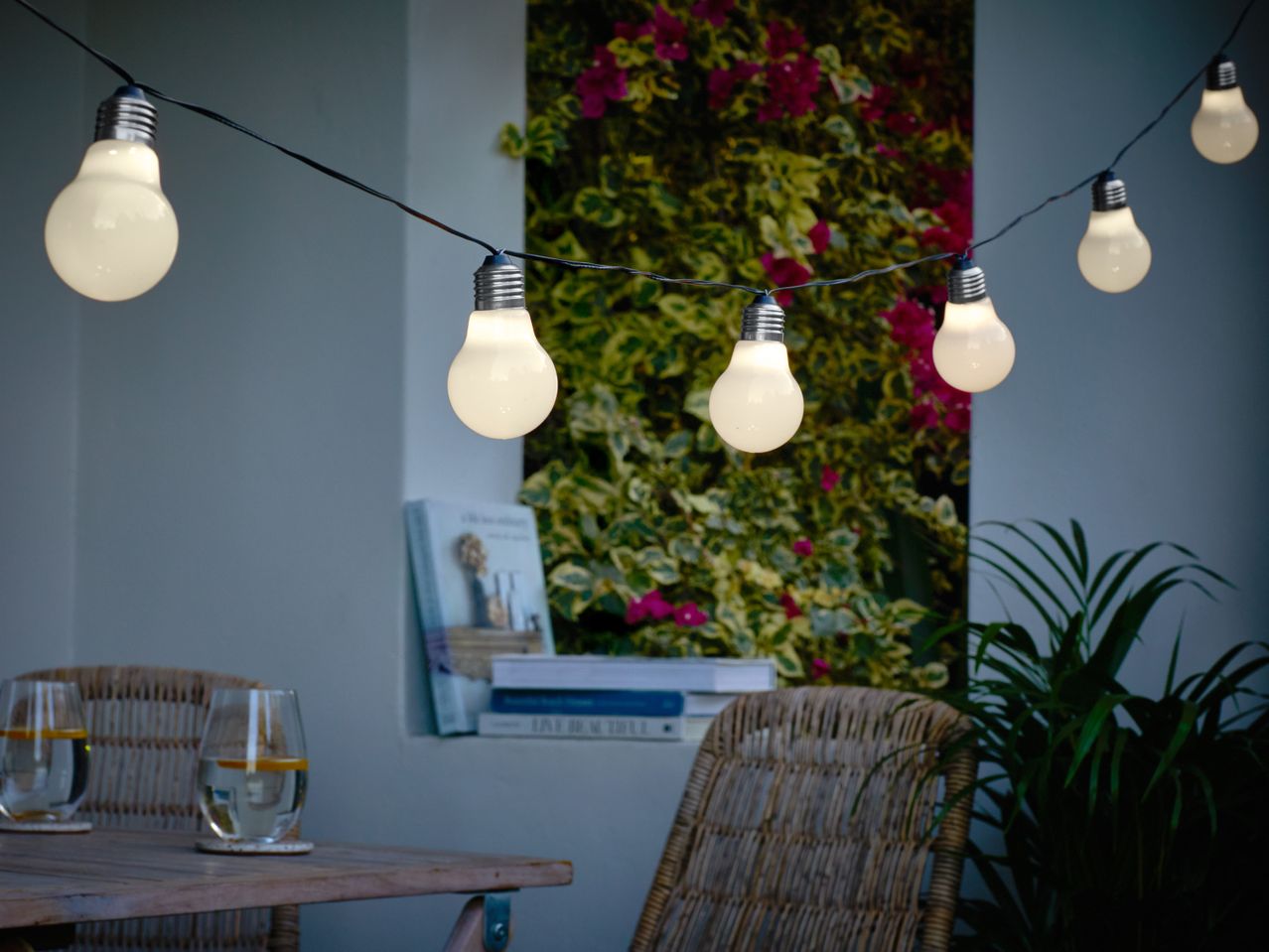 Outdoor string lights illuminate a cozy patio with wicker chairs and drinks on a wooden table.