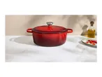 Red cast iron Dutch oven on a white marble surface with olive oil and chili peppers.