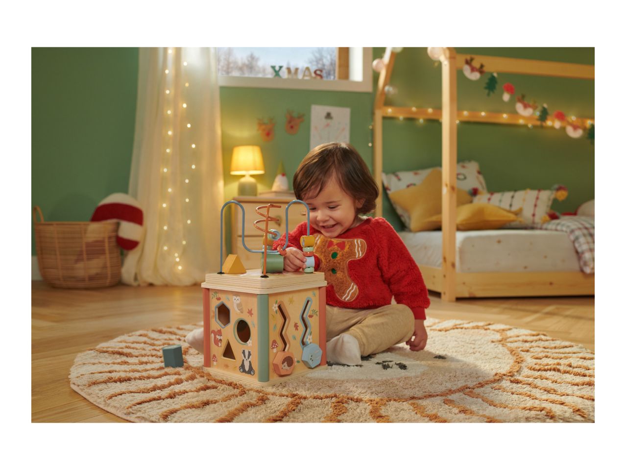 Toddler playing with a wooden activity cube in a festive room with 'XMAS' decor.