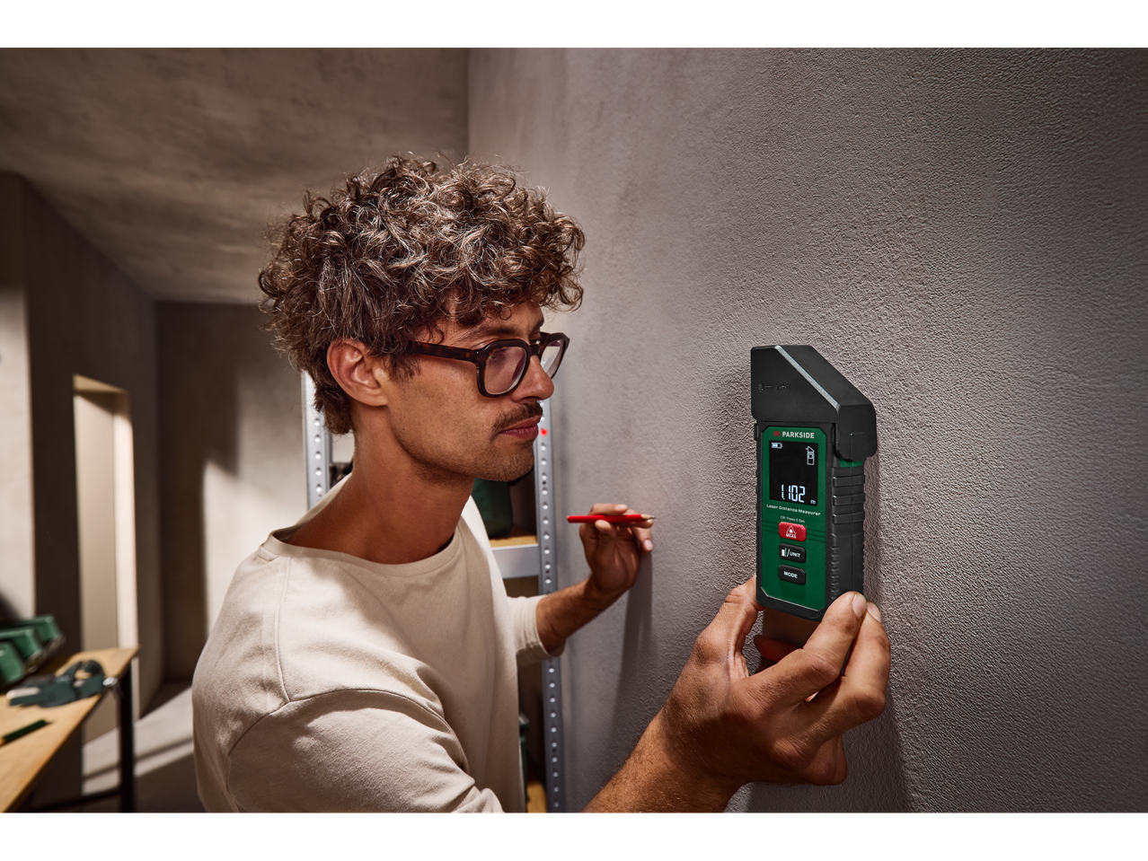 Bărbat folosind un telemetru laser Parkside® 5 în 1 pe un perete, marcând cu un creion.