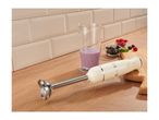 Cream-colored hand blender on a wooden countertop next to a beaker with a berry smoothie