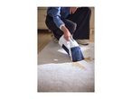 A person cleaning a stain on a light-colored carpet with a handheld carpet cleaner.