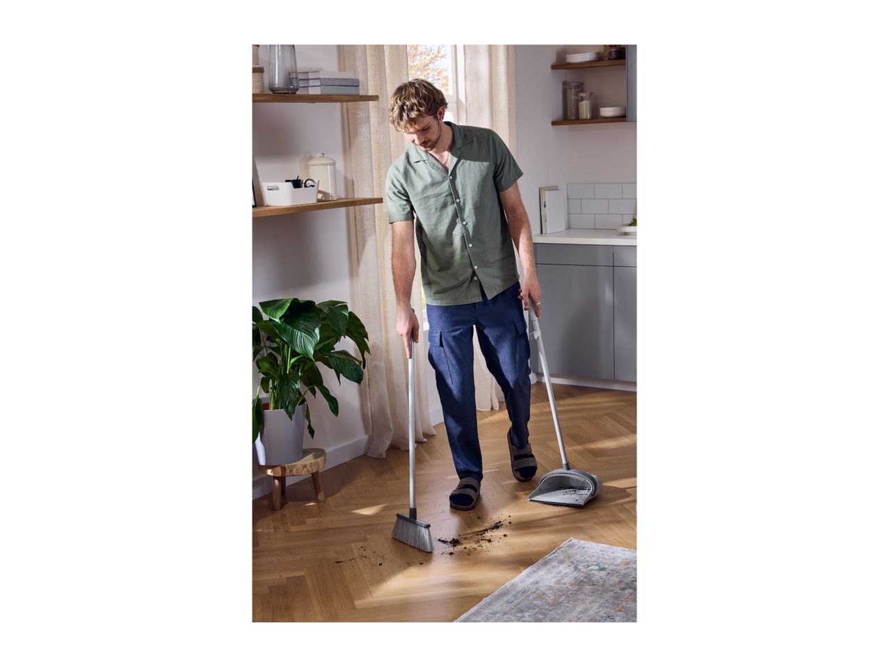 Man sweeping dirt on a wooden floor with a broom and dustpan.