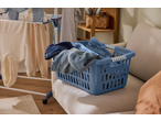 Blue laundry basket filled with denim clothes on a sofa, with a drying rack in the background.