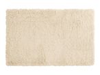 A rectangular, light beige, fluffy bath mat with a shaggy texture.