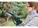 Woman using a Parkside mini chainsaw to prune a tree branch in a garden.